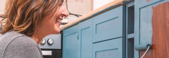 Person streicht Küchenschrank mit Farbrolle.